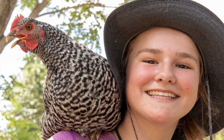 a person with a chicken on their should smiles at the camera during a service project with outward bound